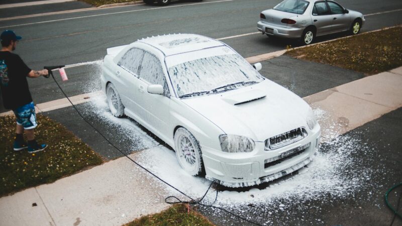 A mobile detailer washing a car with car shampoo he bought in bulk